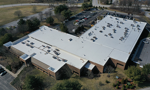 Overview of two commercial warehouses with a gray roof over them, and urban landscape visible behind them